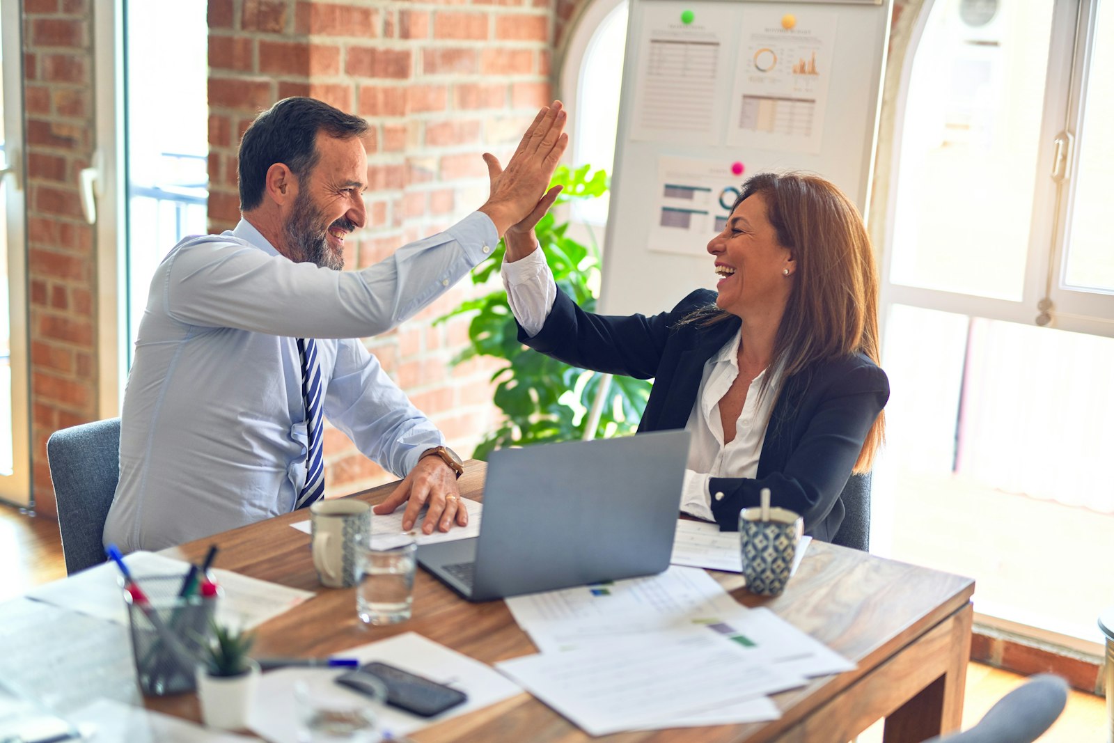 Two colleagues celebrating with a high-five over a laptop in a bright office