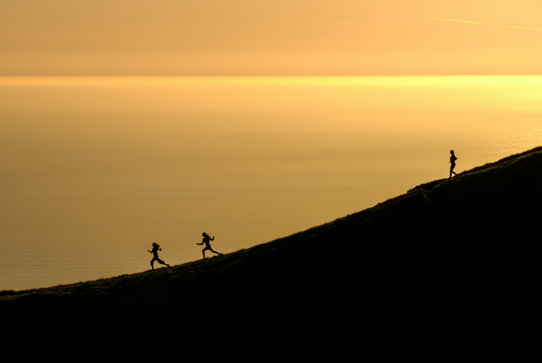 Three trail runners silhouetted on a ridge at golden hour