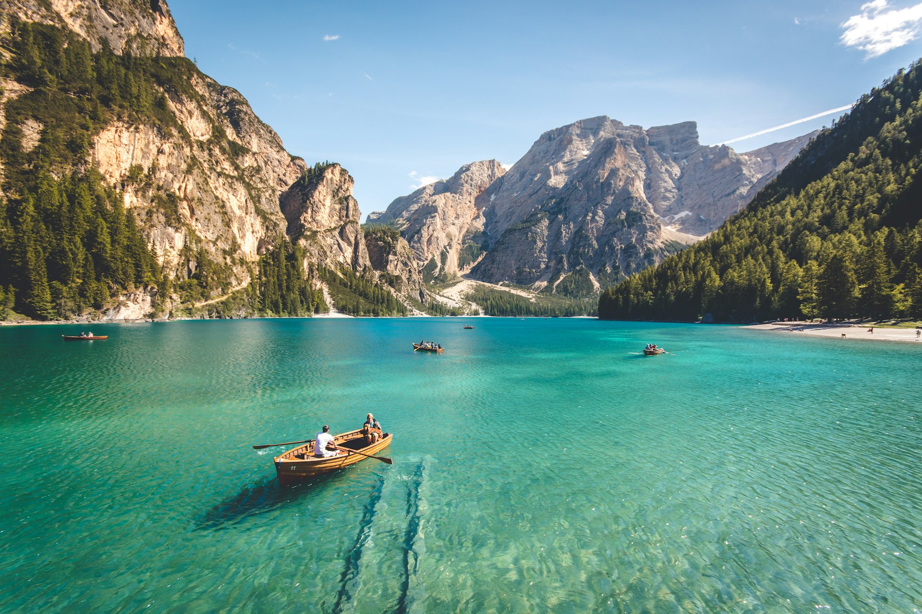 Rowboats on a turquoise mountain lake ringed by forest and peaks